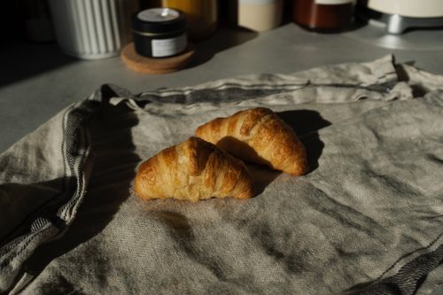 Free Tasty croissants resting on a linen cloth with soft morning light creating a cozy setting. Stock Photo