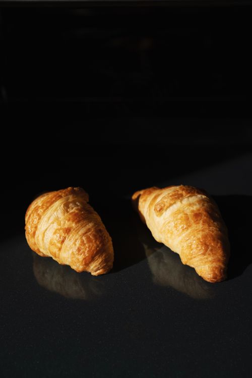 Free Two freshly baked croissants on a reflective dark surface with dramatic lighting. Stock Photo