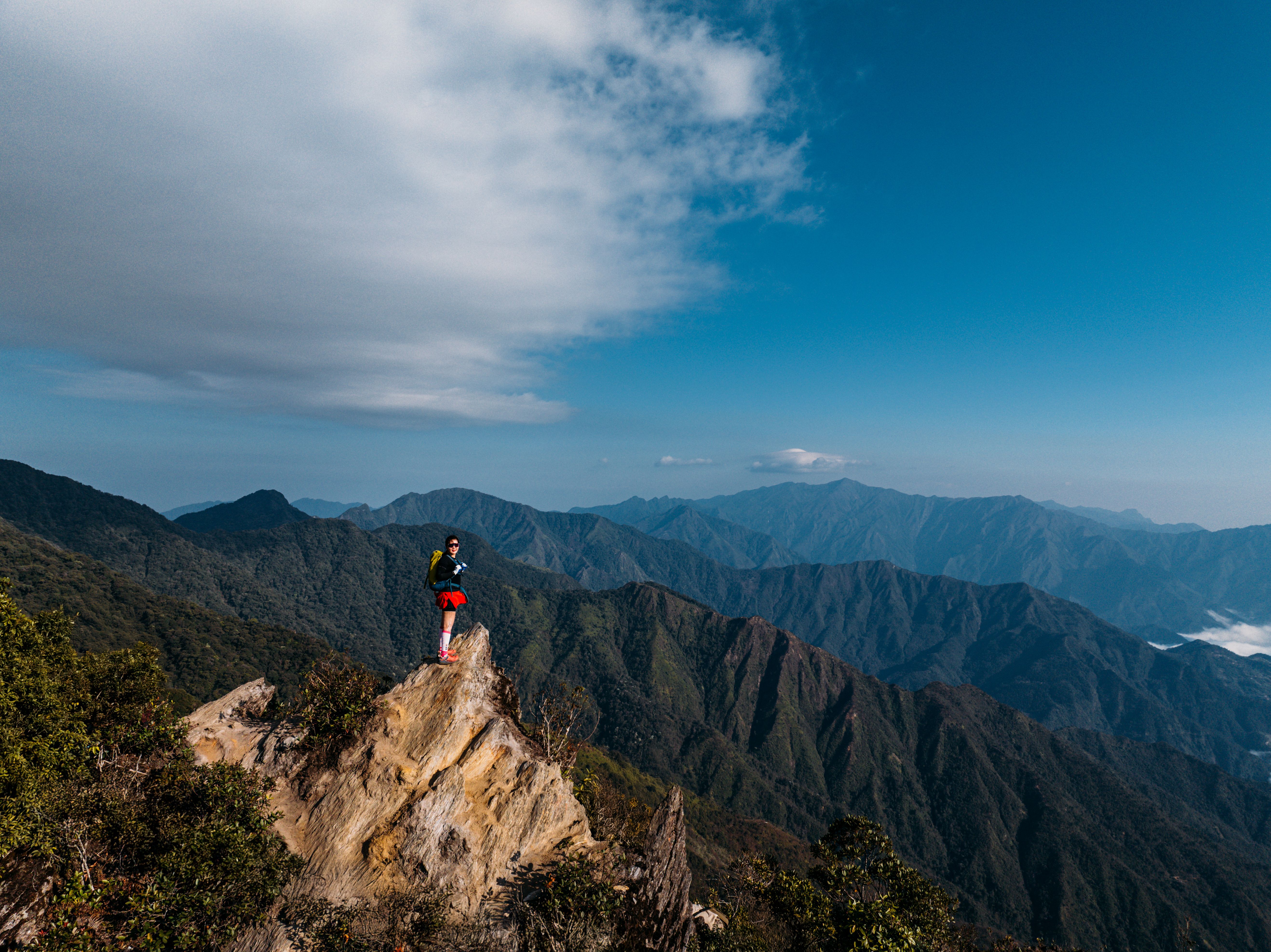 Hiker stands atop a rocky cliff overlooking expansive mountain range in Vietnam.