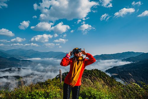 Free Young traveler posing with peace sign on a mountain with clouds and blue sky. Stock Photo