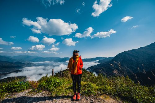 Free Hiker stands on mountain top admiring clouds and blue sky in daylight. Stock Photo