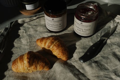 Free Delicious pair of fresh croissants with jars of jam and sauce on crumpled gray tissue Stock Photo