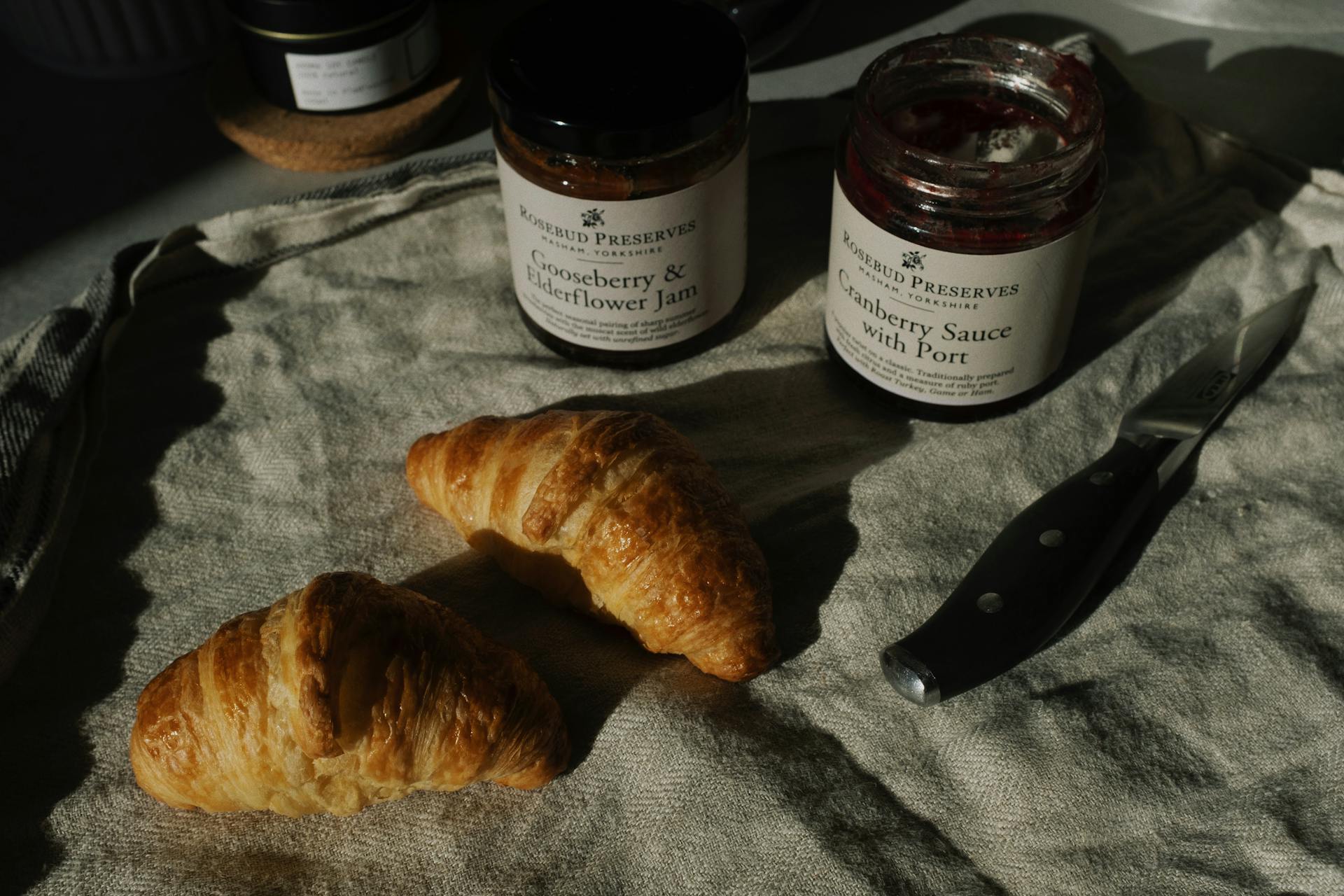 Delicious pair of fresh croissants with jars of jam and sauce on crumpled gray tissue