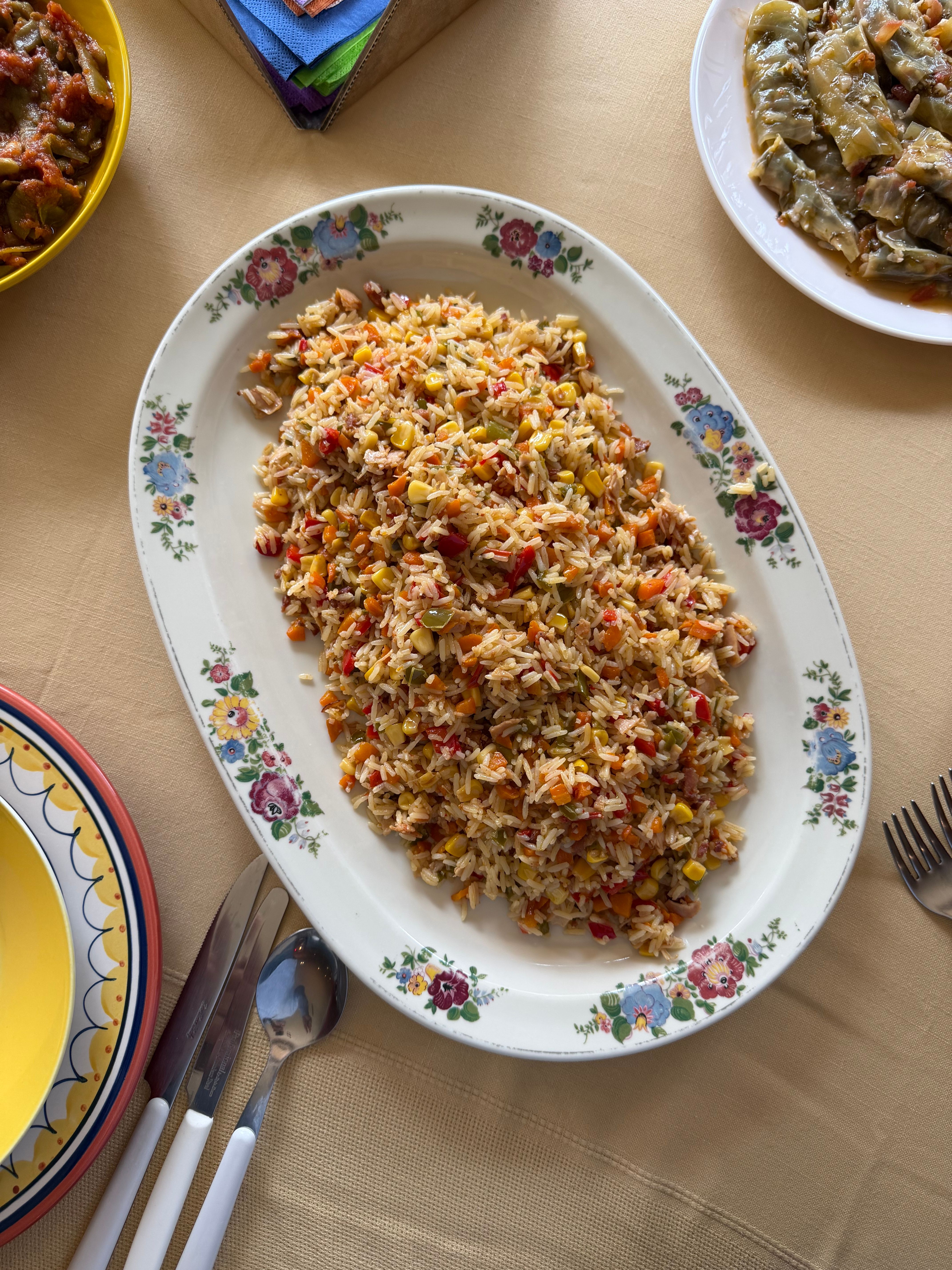 A vibrant vegetable pilaf served on a floral platter, accompanied by side dishes, set on a table.