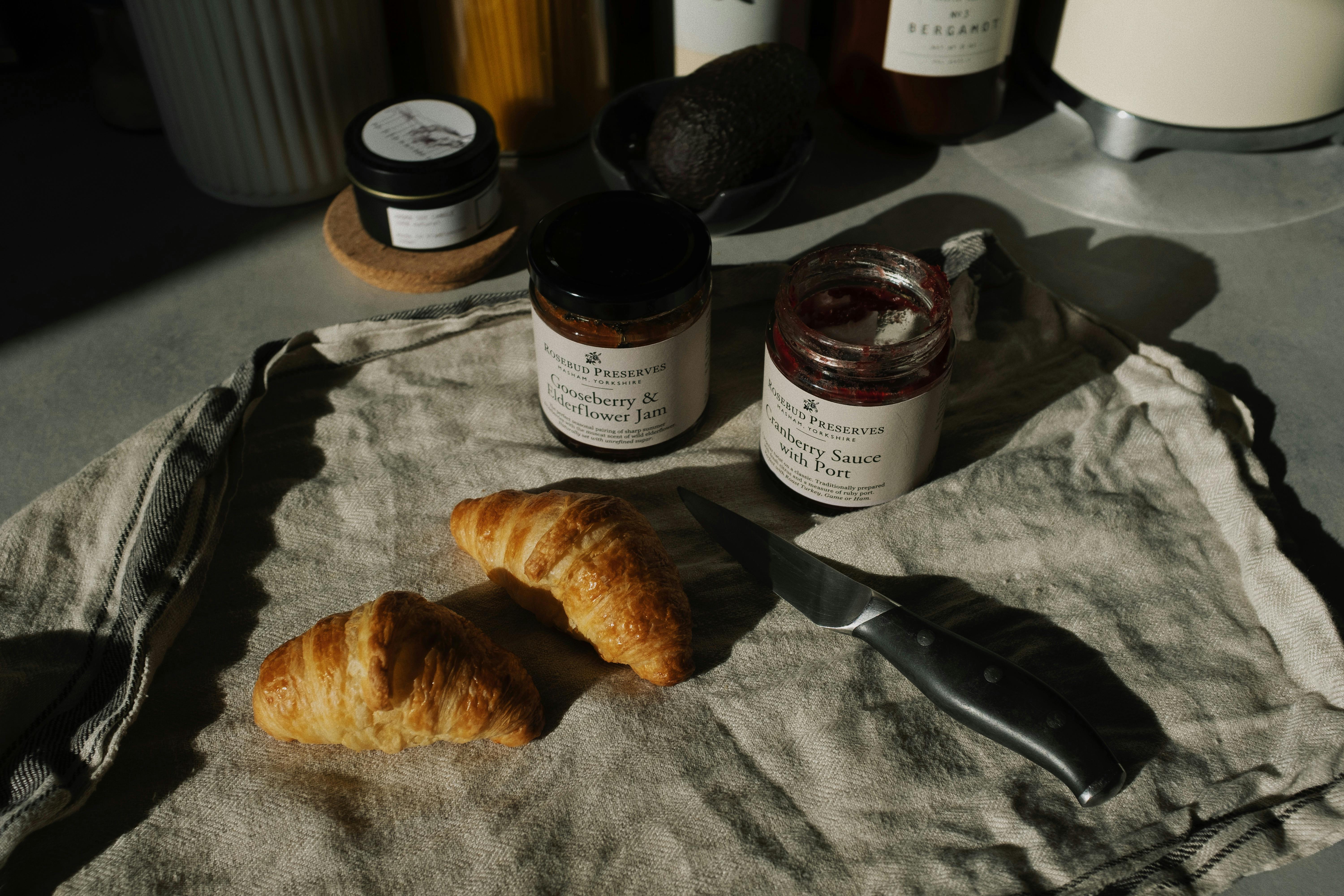 tasty pair of fresh croissants with jars of jam and sauce on crumpled gray tissue