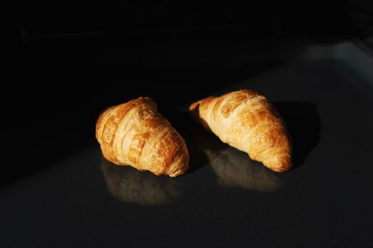 Group of two baked tasty brown crunchy French croissants placed on black glass background