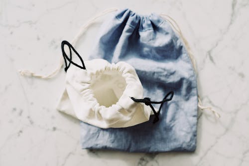 Top view of white and blue fabric eco friendly bags with drawstrings placed nearby on white marble table in light room