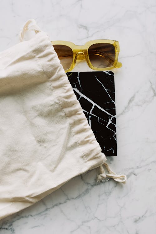 Sunglasses and notepad placed in white bag on marble table