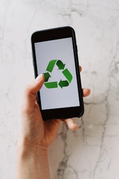 From above view of crop hand showing mobile phone with green recycle icon on white background above marble table