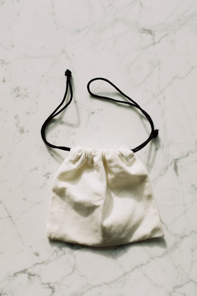 Small White Textile Bag With Black Drawstrings On Marble Table