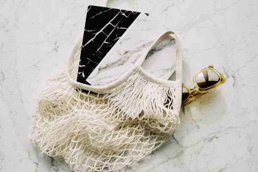 Stylish flat lay featuring eco-friendly mesh bag and sunglasses on a sleek marble surface.