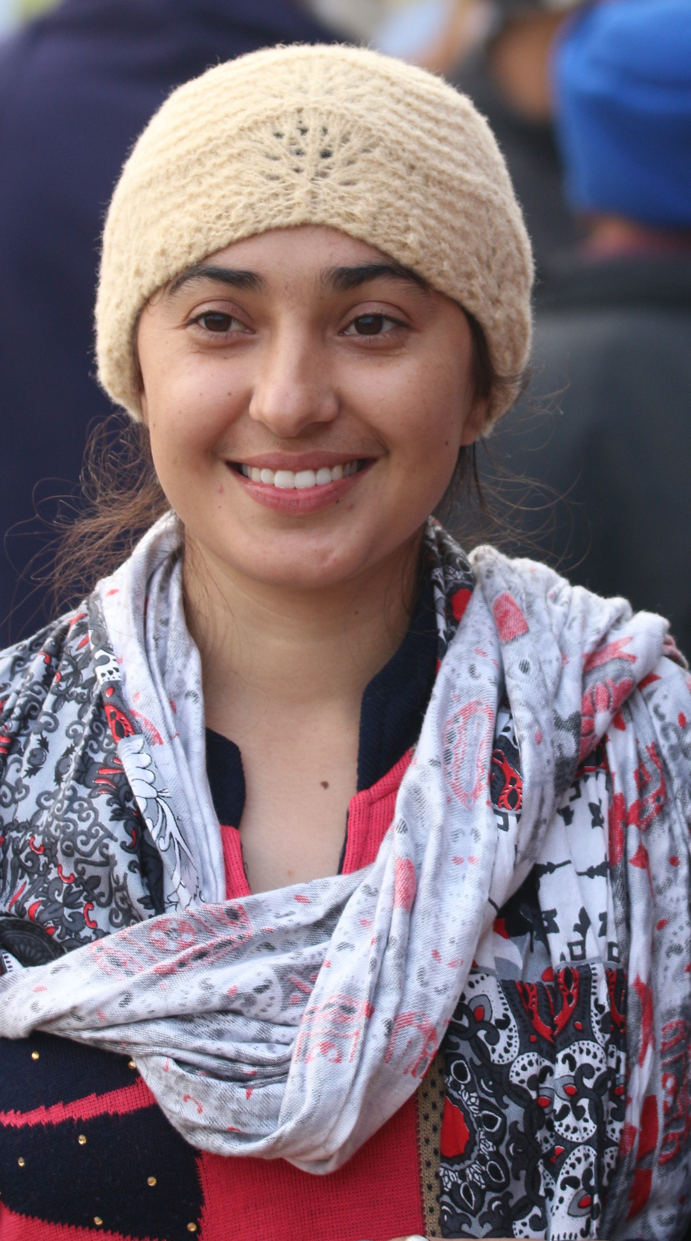 Portrait of a woman wearing a knitted hat and scarf, smiling during a cold day outdoors.