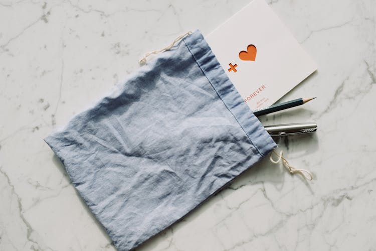 White Postcard With Pen And Pencil In Blue Textile Bag Placed On Marble Table