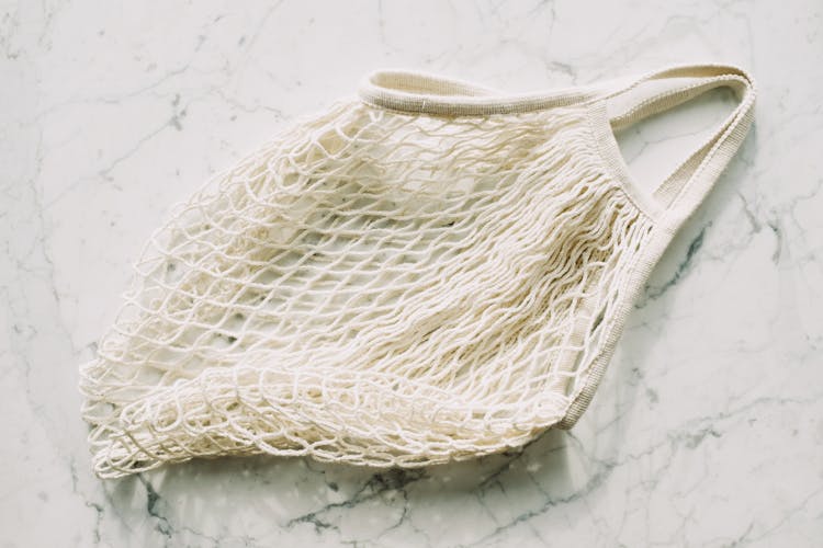 Empty White Textile Mesh Bag Placed On Marble Table In Room