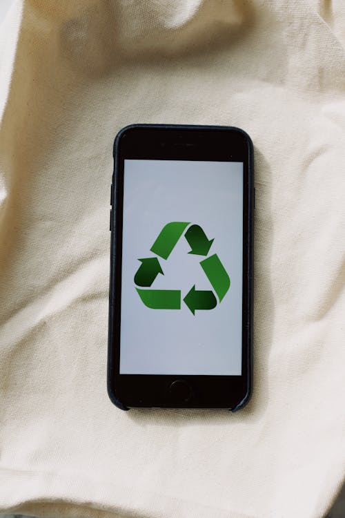 Smartphone with recycling symbol on screen placed on white textile surface