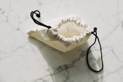 Top view of empty white textile bag with black drawstrings placed on marble table in room