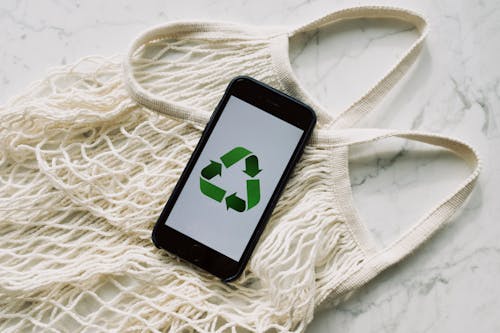 Free Smartphone with recycling sign on screen placed on white mesh bag on marble table Stock Photo