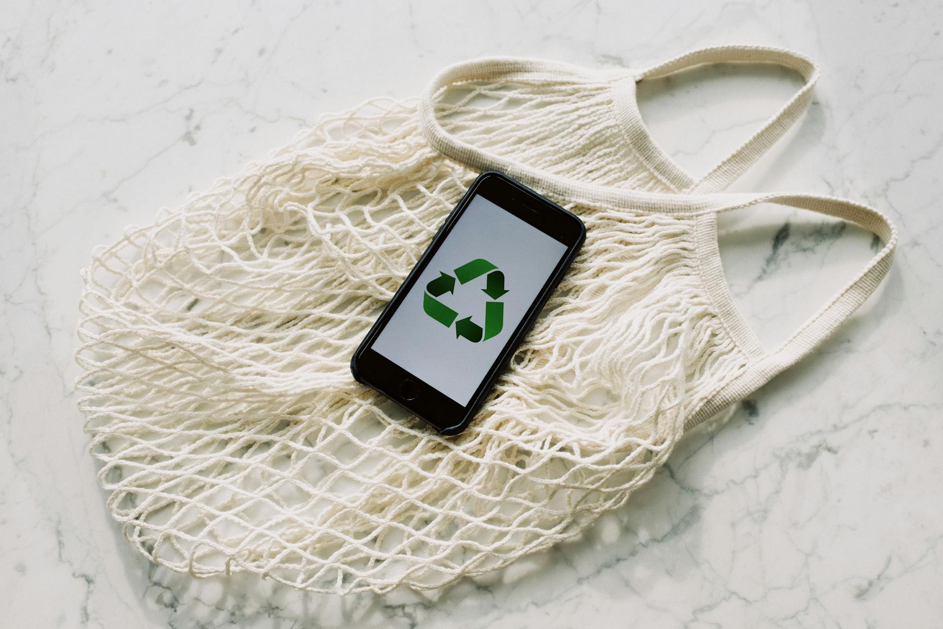 A reusable bag with a phone that shows a recycle sign on it