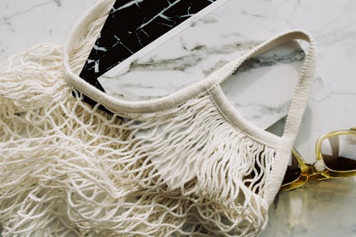 From above view of trendy sunglasses and books in eco friendly cotton mesh bag on marble table in room