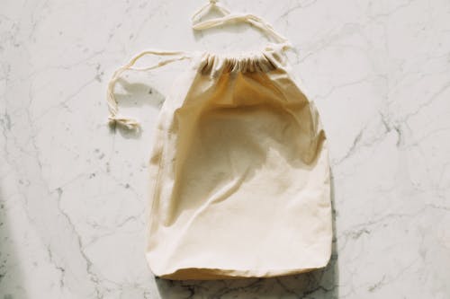 Top view of white empty textile bag with drawstrings placed on marble table in light room