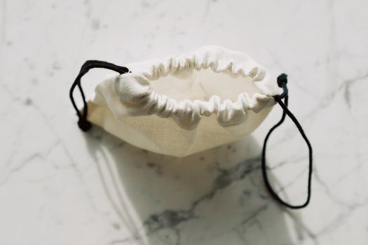 A simple canvas drawstring pouch placed on a marble background, captured in natural light.