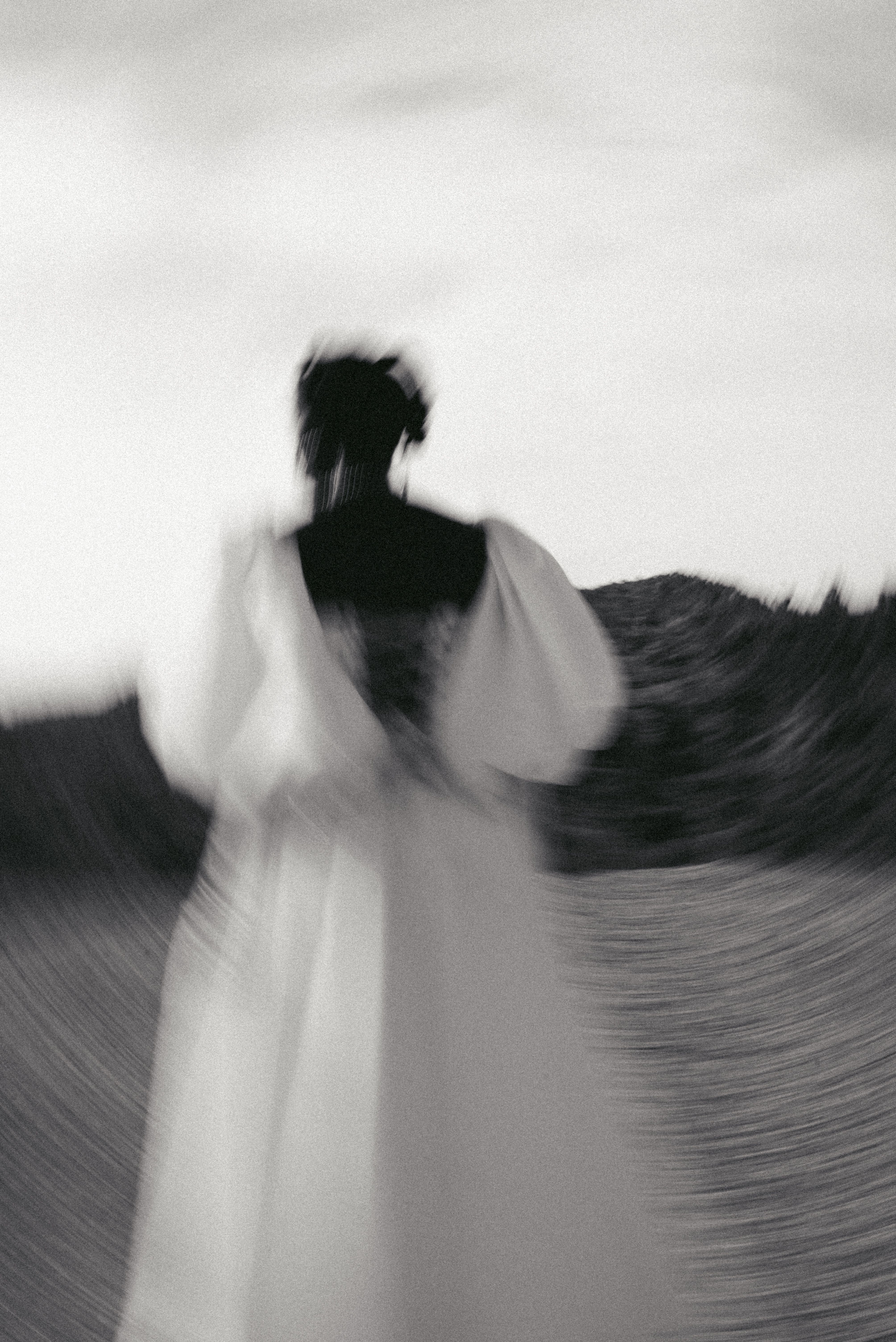 Blurred black and white portrait of a woman in a white gown outdoors.