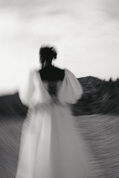 Blurred black and white portrait of a woman in a white gown outdoors.