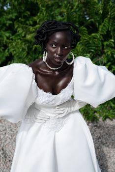 Portrait of a stylish woman posing outdoors in a luxurious white gown with a natural backdrop.