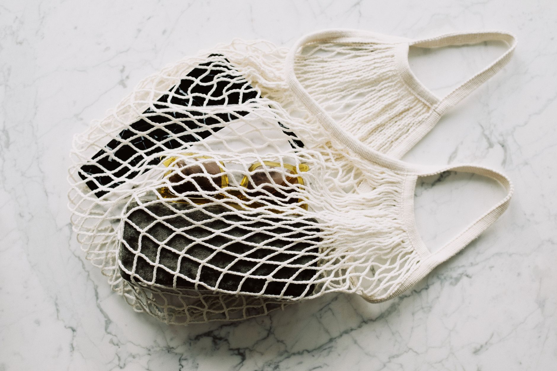 Stylish eco-friendly mesh bag on marble, containing groceries and accessories, perfect for sustainable living.