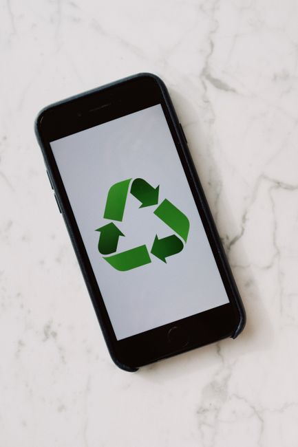 Smartphone placed on marble surface displaying green recycle symbol.