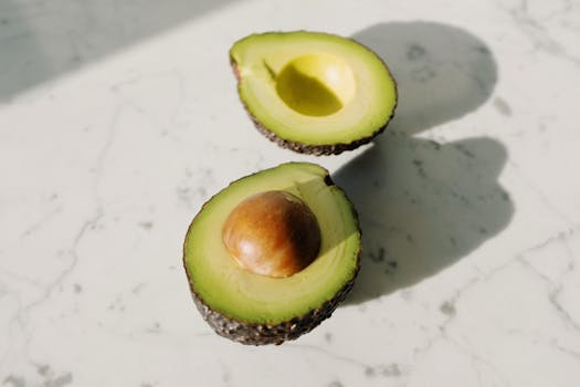 A fresh avocado cut in half, displayed on a marble countertop with natural light.