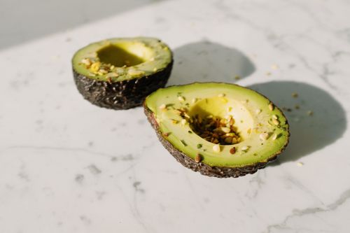 Free From above of fresh green avocado halves without kernels sprinkled with seed mixture placed on white marble desk served for healthy vegetarian breakfast preparation Stock Photo