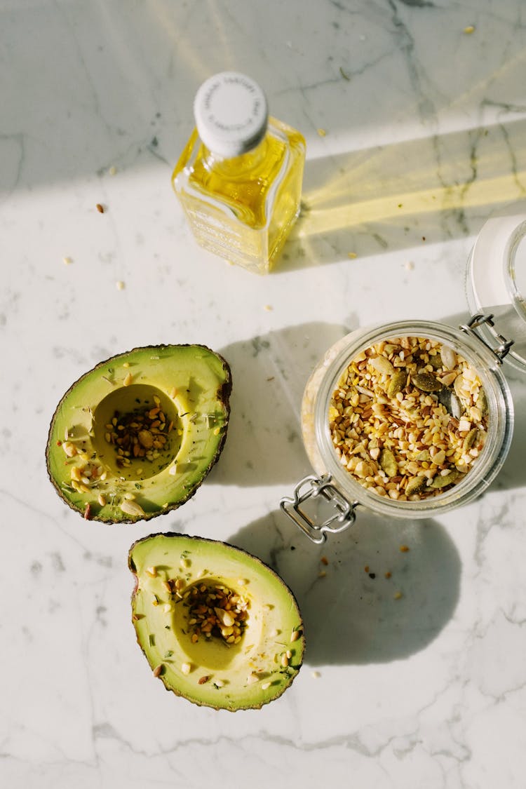 Delicious Halved Avocado With Various Seed Grains And Olive Oil On Marble Surface