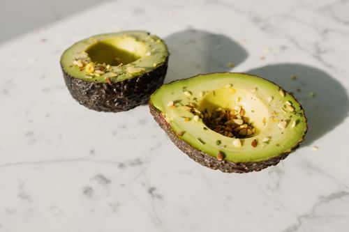 Free From above of fresh green avocado halves without kernels sprinkled with seed mix laying on white marble table ready for healthy vegan breakfast Stock Photo