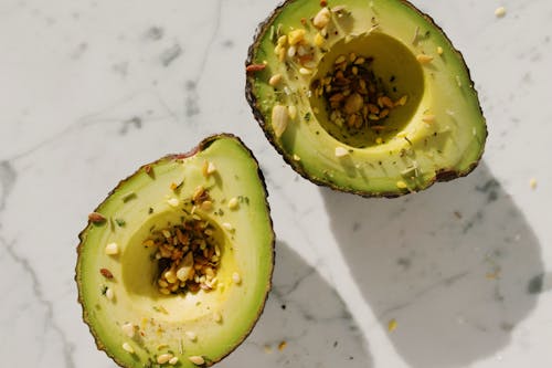 Free Top view of fresh green halved avocado without kernel with seed mixture on them placed on white marble table for healthy vegetarian breakfast Stock Photo