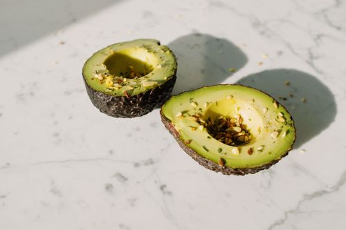 Free From above of green halved avocado sprinkled with various seeds placed on white marble counter served for healthy vegetarian breakfast preparation Stock Photo
