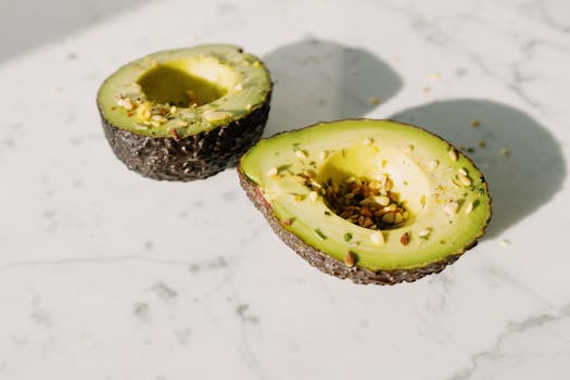 Delicious halved avocado topped with seeds on a clean marble surface, perfect for healthy eating concepts.