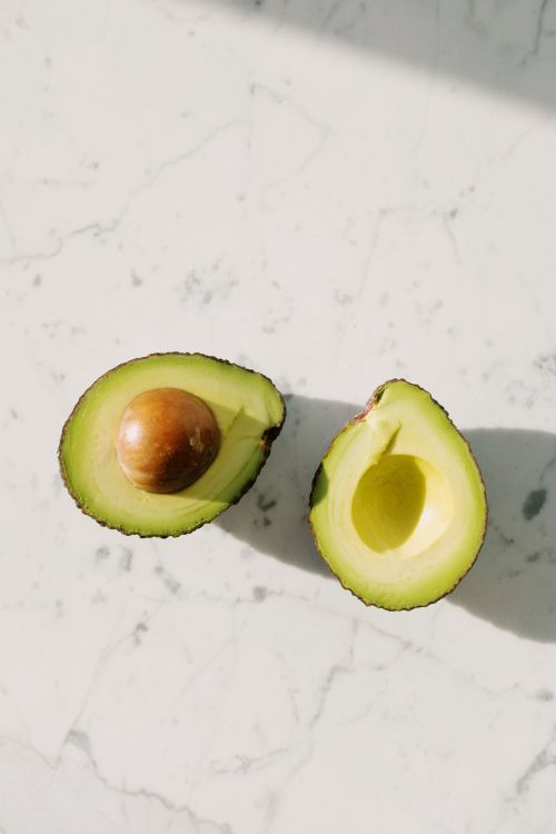Free Sliced avocado halves on a light marble background, showcasing vibrant texture. Stock Photo