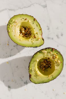 Sliced avocado halves sprinkled with seeds on a white marble background, showcasing healthy food concepts.