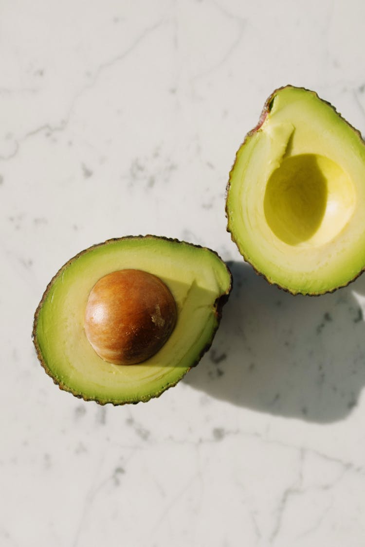 Halves Of Fresh Green Avocado On Marble Surface