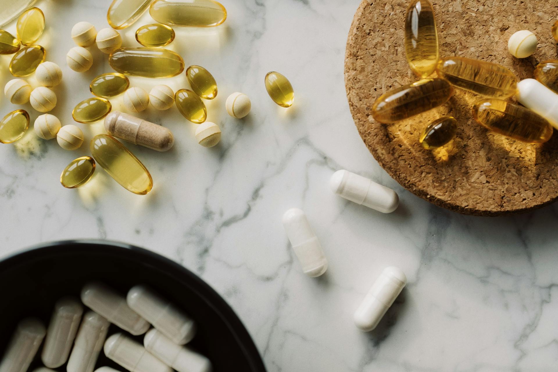 Flat lay of various capsules and pills on marble for healthcare and medication concept.