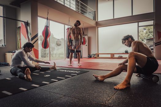 Three men stretching and preparing for a workout session in a modern gym with large windows.