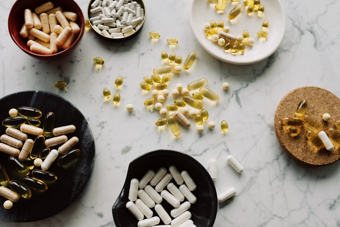 Free From above of various types of medication pills and yellow capsules of omega placed on different plates and stands on table Stock Photo