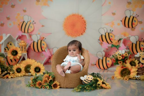 Free Charming photograph of a baby in a cozy chair surrounded by vibrant sunflower and bee decor. Ideal for nursery themes. Stock Photo