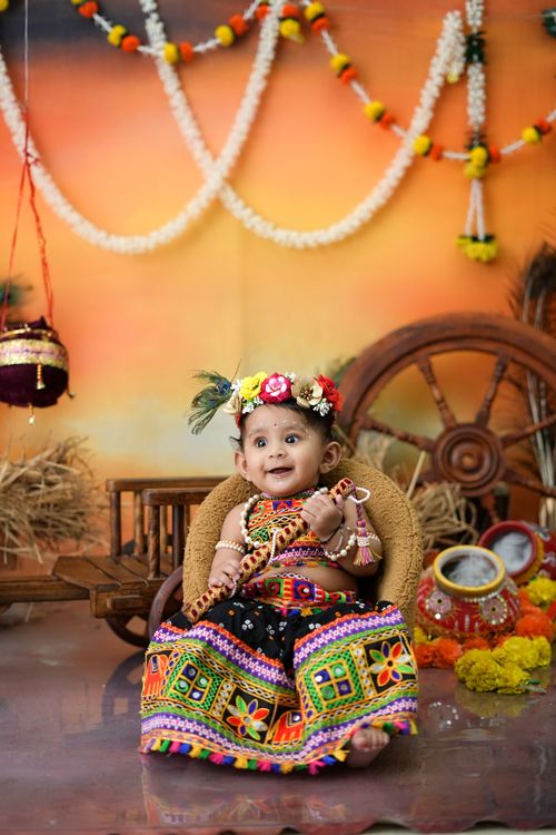 Free A cute baby dressed in colorful traditional attire for a festive photoshoot, sitting amidst vibrant decor. Stock Photo