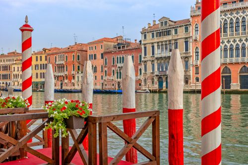 Free A picturesque view of vibrant buildings and iconic poles along a canal in Venice, Italy. Stock Photo