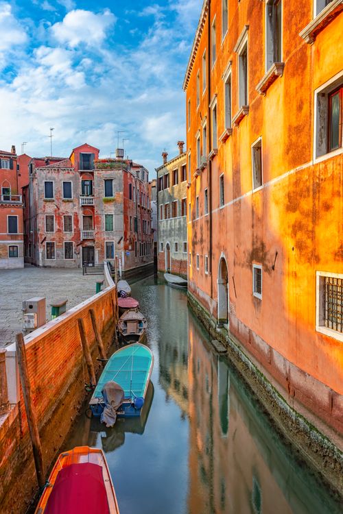 Free Picturesque scene of a Venetian canal reflecting colorful buildings and boats at dawn. Stock Photo