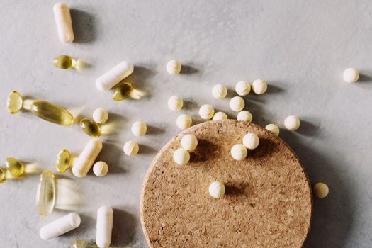 A mix of various capsules and pills scattered on a cork surface, depicting healthcare and wellness.