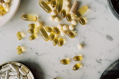 Top view of various vitamins in gelatin shell arranged on marble tabletop between different plates with drugs during photo shoot