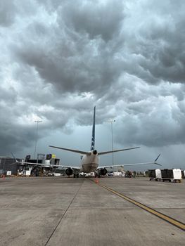 Airplane parked on tarmac under a dark, stormy sky, showcasing striking contrast.